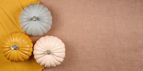 Obraz premium Three pastel colored pumpkins rest on a textured brown background and a vibrant yellow cloth, evoking the warm and inviting atmosphere of autumn and the halloween season