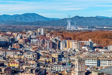 Panoramic view of Girona with densely packed buildings, mountains, and forests. The cityscape blends historic, modern, and industrial architecture in Catalonia, Spain