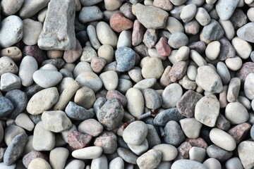 Close-up view of small pebbles creating a natural pattern and texture. Tiny gravel stones in various earthy tones form a seamless background, ideal for use in design or nature-themed projects.