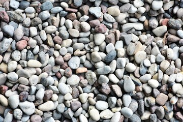Close-up view of small pebbles creating a natural pattern and texture. Tiny gravel stones in various earthy tones form a seamless background, ideal for use in design or nature-themed projects.