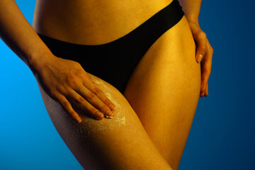 Hand Applying Exfoliating Scrub To A Woman's Leg On Blue Background