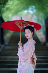 A young Asian Japanese woman in a Traditional Furisode Kimono Yukata dress costume holding a red...