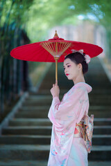 A young Asian Japanese woman in a Traditional Furisode Kimono Yukata dress costume holding a red...