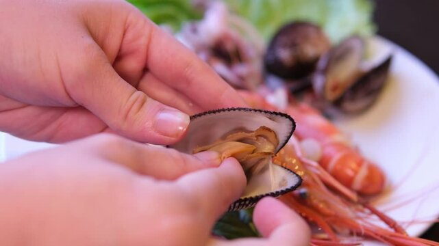 The hand opens and removes the meat from the steamed clam shell, revealing the tender meat inside, with a bowl of clam meat gathered in the background, illustrating the moment of seafood preparation.