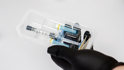 A professional cosmetologist wearing gloves prepares a syringe filled with a medicinal solution in...