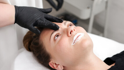 Esthetician applying numbing cream on patient's lips before injects filler.