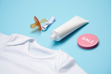 Baby essentials arranged on a vibrant blue background, featuring a white onesie, pacifier, cream tube, and a pink sale tag, showcasing a playful and inviting atmosphere for parents