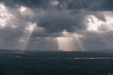 Dramatic sun rays filtering through dark clouds, illuminating a vast and picturesque landscape in...