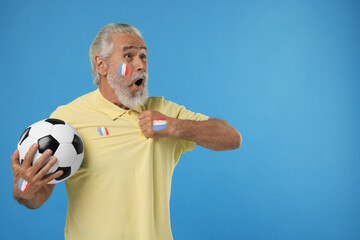 Excited fan with flags of France painted on his body and polo shirt holding soccer ball against...