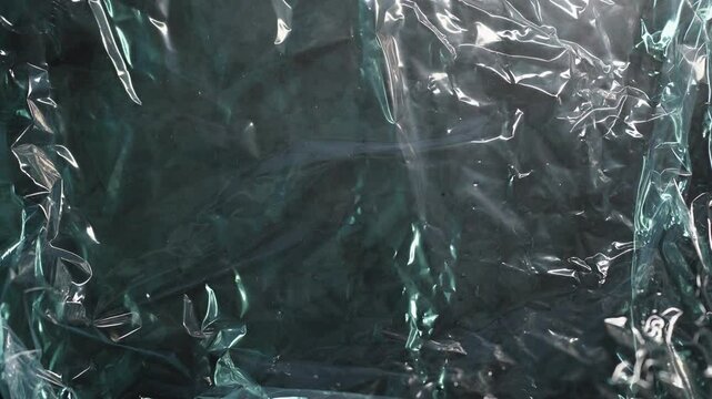 Crumpled plastic cling film texture on black background with moving lighting