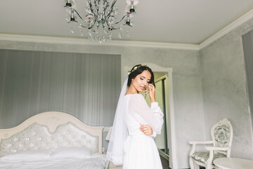 A bride stands in a soft light vintage bedroom, feeling calm and reflective. The elegant white...