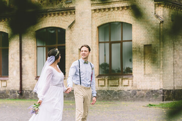 Newlywed couple walking hand in hand in front of an old building, expressing love, joy, and...