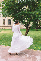 Happy bride twirling in her white dress on a summer wedding day, enjoying freedom and motion outdoors with green garden background and natural light.
