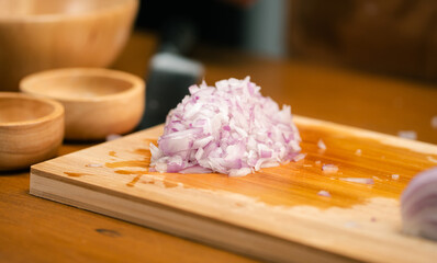 Close up of Asian man's hands cutting onions on a wooden cutting board in a kitchen, preparation...