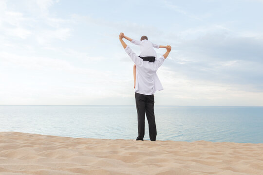 A father carries his son on his shoulders on a tranquil beach overlooking the ocean. Perfect for themes of family, love, parenting, summer, and childhood memories.