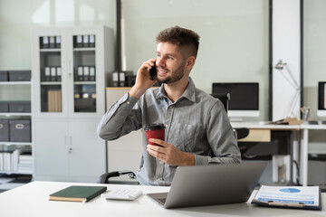 Naklejka premium Smiling caucasian young freelancer working from office remotely. He is talking on the phone.