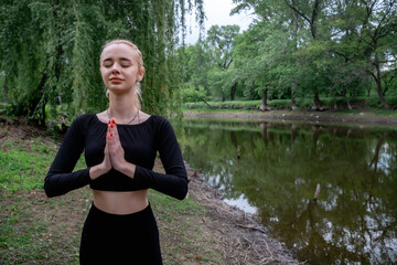 Young woman meditates in nature with palms together in Anjali Mudra, radiating calm and focus.