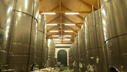 interior of a modern winery showcasing large stainless steel fermentation tanks under a wooden ceiling, highlighting the winemaking process and industrial design