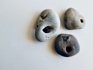Three naturally holed stones, also known as hag stones or witch stones, on a white background. Believed to bring protection and good luck. Found by the sea.