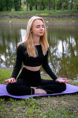 A young, attractive blonde woman meditates in nature, radiating peace and inner harmony.