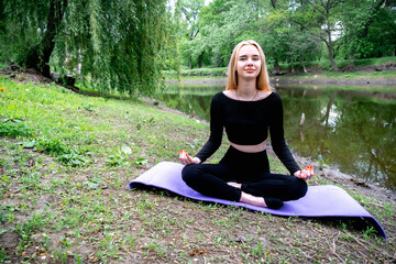 A young, attractive blonde woman meditates in nature, radiating peace and inner harmony.