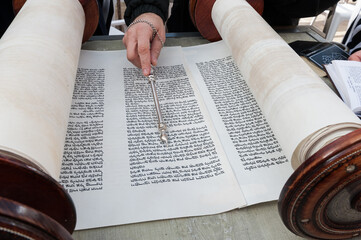 Closeup of bar mitzvah boy reading the Torah and using a yad or pointer to guide him through the...