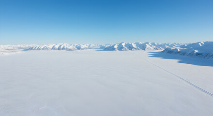 A vast expanse of snow-covered land stretches towards distant mountains under a clear blue sky.