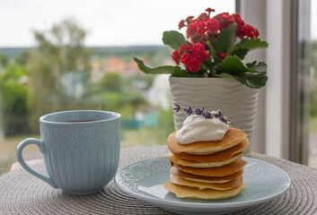 breakfast on the table, pancakes, fritters, pancakes with sour cream and lavender flowers on a plate, a cup of coffee and a vase of flowers on the table