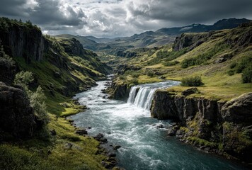Fototapeta premium Majestic waterfall cascading down rocky cliffs surrounded by lush greenery and dramatic moody sky in Icelandic wilderness landscape