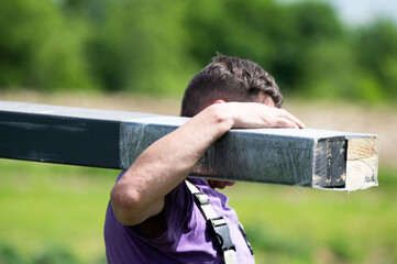A man carries a wooden beam for installing a gazebo in a lavender field.