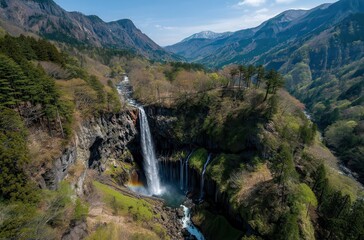 Fototapeta premium Majestic Waterfall Cascading Through Lush Green Forests Surrounded by Mountains Under Clear Blue Sky With Snow-Capped Peaks in Distance