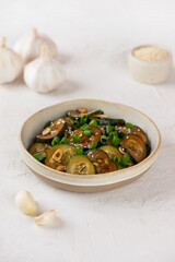 Green cucumbers salad with sesame seeds, green onion, soy sauce and garlic in a bowl. Vertical orientation.