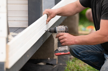 The builder attaches the wall to the gazebo frame using screws and a screwdriver.