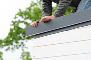 A man holds a metal sheet in his hands to attach to the edge of the roof.