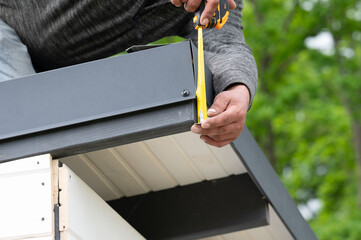The craftsman measures the length of the metal cladding at the edge of the roof.