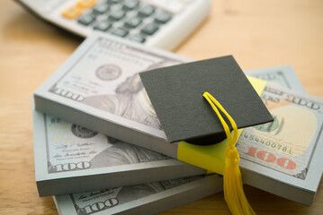 Graduation cap university or college degree on stack US dollar banknotes. Education expense budget plan of money savings, student loan or debt, personal loan, scholarship for studying abroad concept.