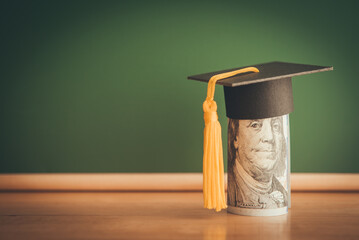US dollars banknote wears graduation cap chalkboard background in classroom. Education expense budget plan of money saving, student loan or debt, personal loan, scholarship for studying abroad concept