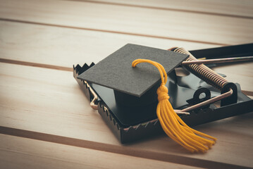 Graduation cap in a rat trap on wooden table background. College or university degrees are not important in future, education loan and unemployment or jobless rate problem, digital disruption concept.