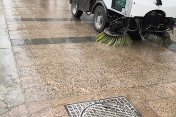 A vacuum utility truck washes the sidewalk.