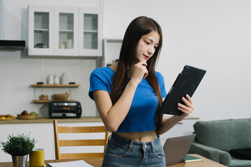 Smiling young Asian woman using digital tablet at home, enjoying remote work or online...