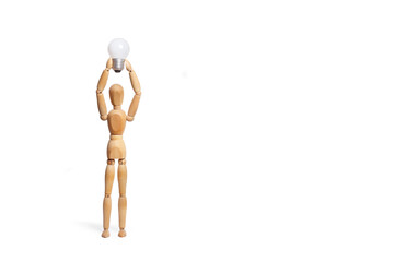 A wooden toy mannequin holding a light bulb with his hands overhead on white background