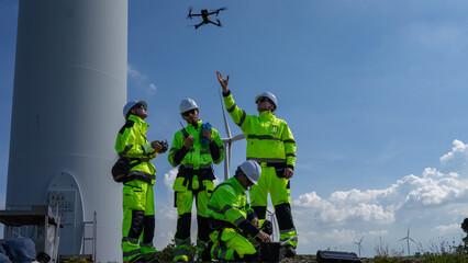 Maintenance engineer team standing at windmills at wind turbine farm. Group of people wear safety...