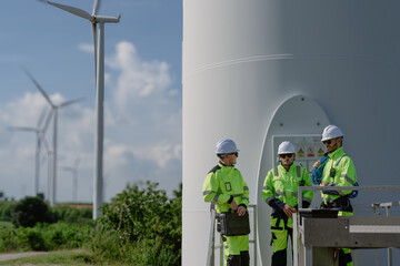 Maintenance engineer team standing at windmills at wind turbine farm. Group of people wear safety...