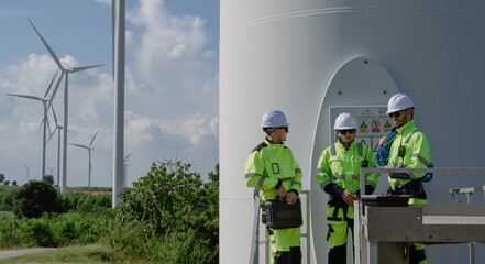 Maintenance engineer team standing at windmills at wind turbine farm. Group of people wear safety...