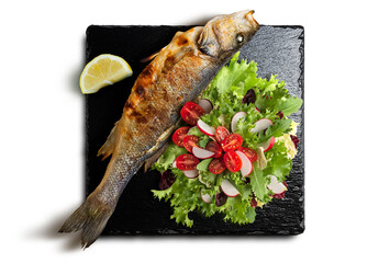Grilled sea bass with mixed salad and lemon on black stone