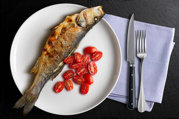 Plate with grilled sea bass and tomatoes with napkin and cutlery