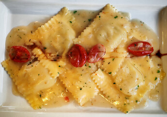 Top view of Rectangular plate with ravioli in sauce and tomatoes