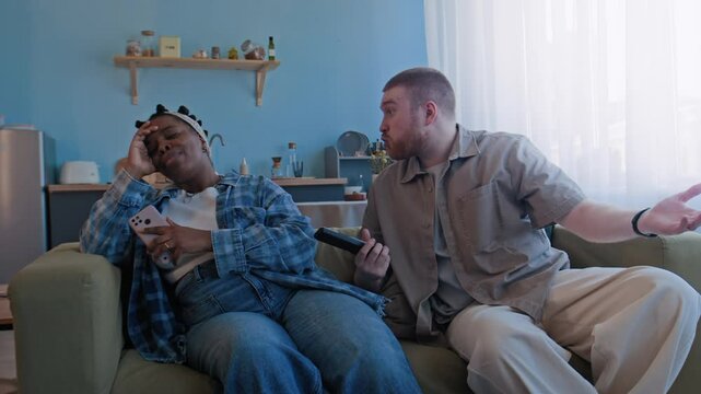 Jealous Caucasian man nagging his African American wife for using social media while sitting on sofa