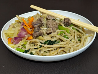 Rich, flavorful stir-fried udon noodles served on a white plate, accompanied by tender pieces of...