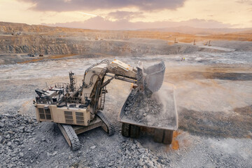Open pit mining industry, aerial top view. Industrial excavator loading ore into big yellow truck...